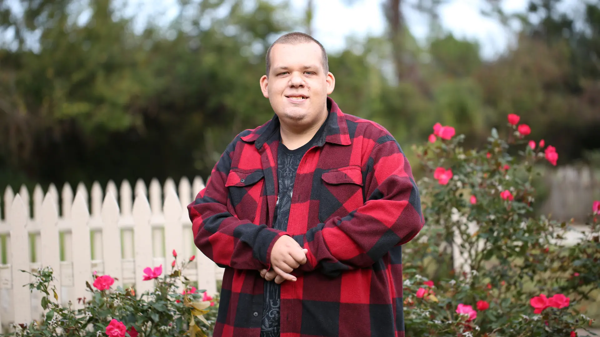 Neuro diverse person in colourful checked jacket smiling to the camera in a rose garden